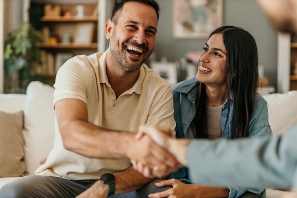 Man shaking hands with an addiction coach while his wife looks on, relieved and hopeful during post-treatment support.